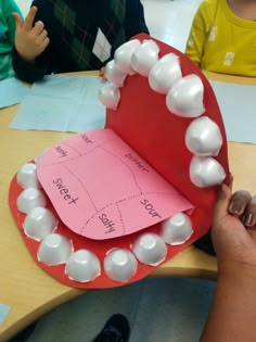 a child's hand is holding up a paper heart with white beads on it