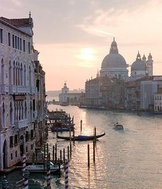 the sun is setting in venice, italy as boats go down the water near buildings