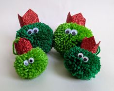 three green and red pom - poms with googly eyes on white surface