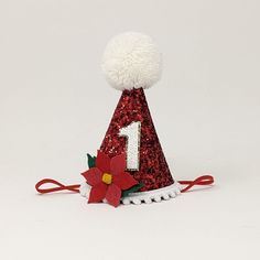 a red and white party hat with a poinsetti on the top that says 1