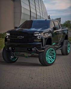 a black truck with green wheels parked in front of a building