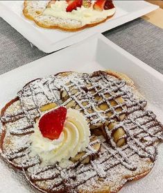 two white plates topped with waffles covered in powdered sugar and strawberries