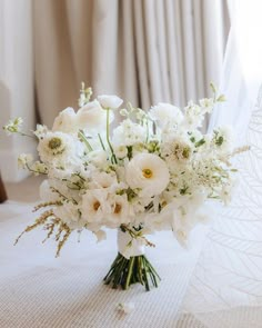 a bouquet of white flowers sitting on top of a table next to a window with curtains