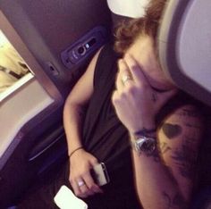 a man with tattoos on his arm sitting in an airplane holding a cell phone to his ear