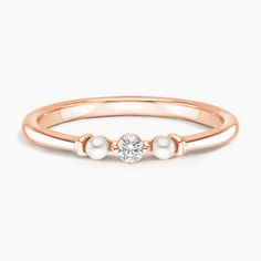 a rose gold ring with two pearls on the side and a diamond in the middle