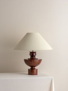 a table lamp sitting on top of a white table next to a wooden bowl with a cream shade