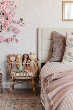 a bed with pink flowers on the wall next to a basket full of baby toys