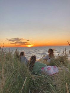 three women sitting on the beach watching the sun set over the water and sand dunes