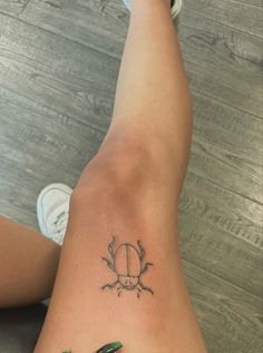 a woman's leg with a tattoo on it and a green beetle sitting on top of her legs