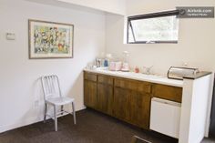 a white chair sitting next to a sink in a kitchen under a painting on the wall