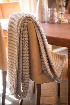 a knitted blanket sitting on top of a wooden table next to a beige chair