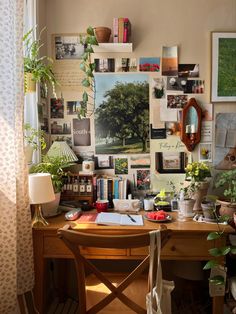 a wooden desk topped with lots of books and plants next to a window covered in pictures