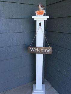 a welcome sign hanging from the side of a house with a bird perched on it