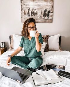 a woman sitting on her bed holding a coffee cup and looking at the camera with both hands in front of her face