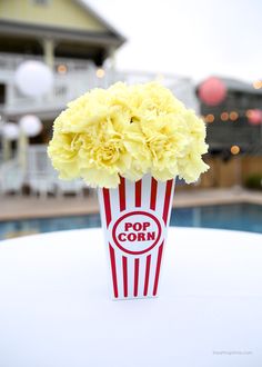 a popcorn box with flowers in it sitting on a table next to a swimming pool