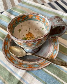 a cup and saucer with spoons sitting on a striped tableclothed place mat