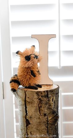 a small stuffed animal sitting on top of a wooden stump next to the letter i