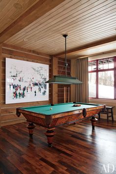 a pool table in the middle of a room with wood flooring and large windows