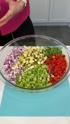 a woman standing in front of a glass bowl filled with chopped onions and bell peppers