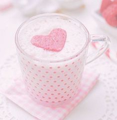 a pink heart shaped drink in a glass mug on a doily with other cupcakes behind it