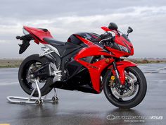 a red and black motorcycle is parked on the pavement in front of an empty parking lot