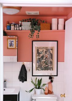 a bathroom with pink walls and white tiled flooring, plants on the shelf above the toilet