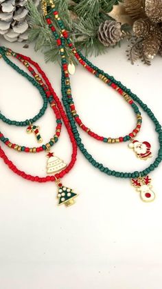 two red and green beaded necklaces with bells on them next to pine cones