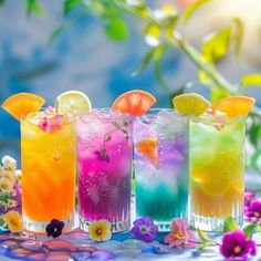 four different colored cocktails are lined up on a table with flowers and greenery