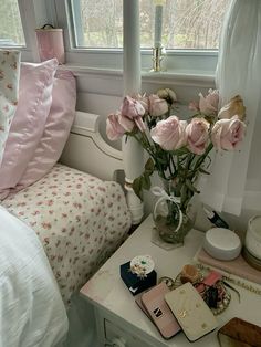 pink roses in a vase on a small table next to a bed