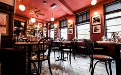 the interior of a restaurant with red walls and wooden tables, chairs, and pictures on the wall