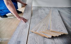 a man laying wood on the floor with his hands and fingers in front of it