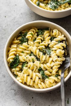 two bowls filled with pasta and spinach on top of a white counter next to a silver spoon