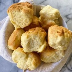 a white bowl filled with biscuits sitting on top of a marble counter next to a napkin