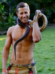 a shirtless man holding a snake in his right hand and smiling at the camera