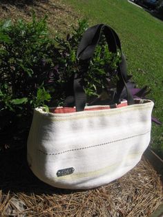 a white bag sitting on top of a pile of hay next to a bush and grass