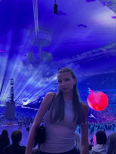 a woman standing in front of a crowd at a sporting event with lights on the ceiling