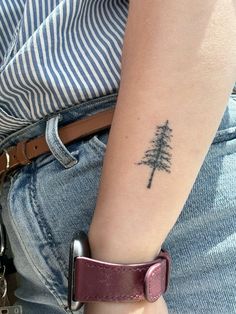 a small pine tree tattoo on the left arm and right arm wristband is shown