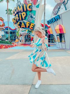 a woman in a tie dye dress is dancing on the sidewalk near a sign that says comic strip cafe