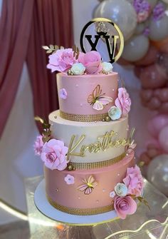 a three tiered cake with pink flowers and gold trimmings on a table