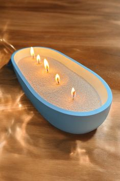 candles are lit in a blue bowl on a wooden table with water droplets around it