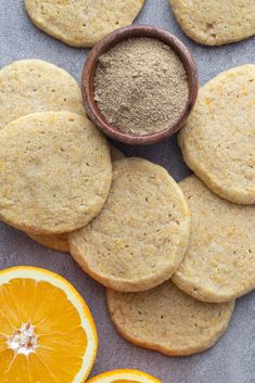 oranges and cookies are arranged next to each other on a gray surface with a bowl of powder