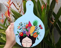 a person holding up a blue cutting board with flowers and pineapples on it