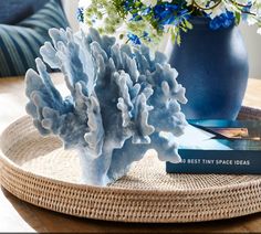 a blue vase filled with flowers next to a book on top of a wicker table