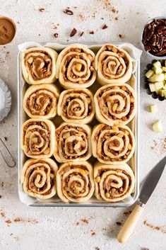 several cinnamon rolls in a baking dish next to some nuts and other ingredients on a white surface