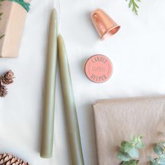 two candles and some pine cones are on the table next to wrapping paper with evergreen leaves