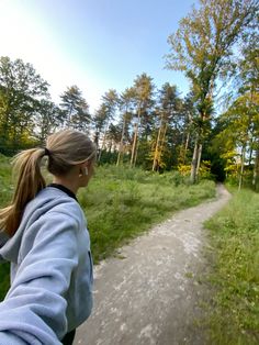 a woman riding on the back of a motorcycle down a dirt road next to a forest