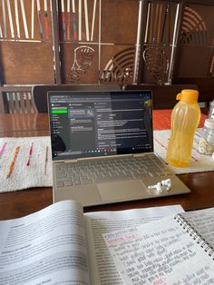 an open laptop computer sitting on top of a wooden table next to a book and water bottle