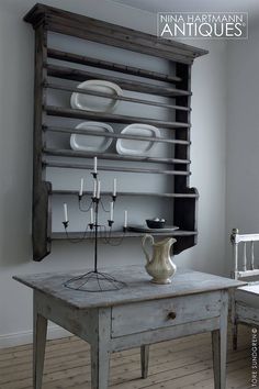 an old wooden table with plates on it and a white vase sitting on top of it