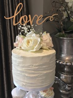 a white wedding cake with flowers and the word love on top