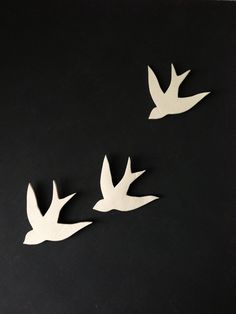 three white birds flying in the air on a black surface with one bird upside down